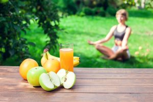 Frau macht Yoga auf einer Wiese. Obst und Getränk im Vordergrund im Vordergrung