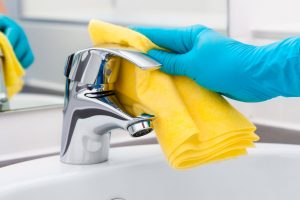 Hand mit Handschuh an und gelbem Lappen in der Hand putz Badezimmeramatur