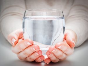 Hände die ein Glas mit klarem Wasser halten