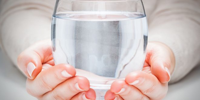 Hände die ein Glas mit klarem Wasser halten